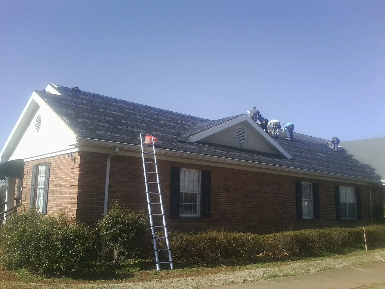 Crew tearing shingles off a brick ranch roof with a ladder set — Metal Roof Repair work by our crew in Prescott