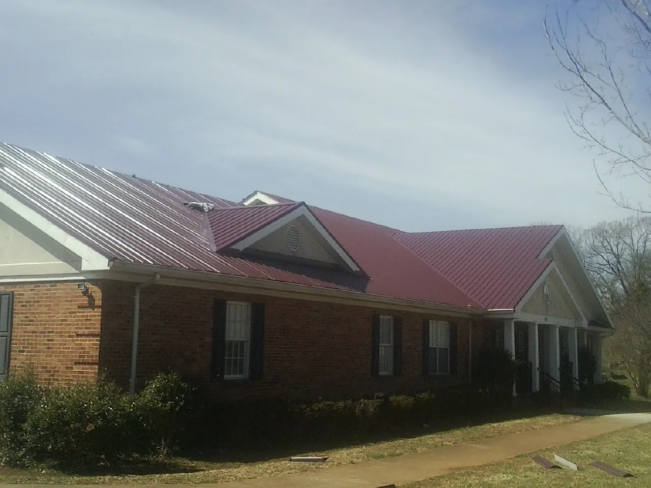 Red metal roof with gabled entries on a long brick building, from a Hail Damage Roof Repair job in Prescott
