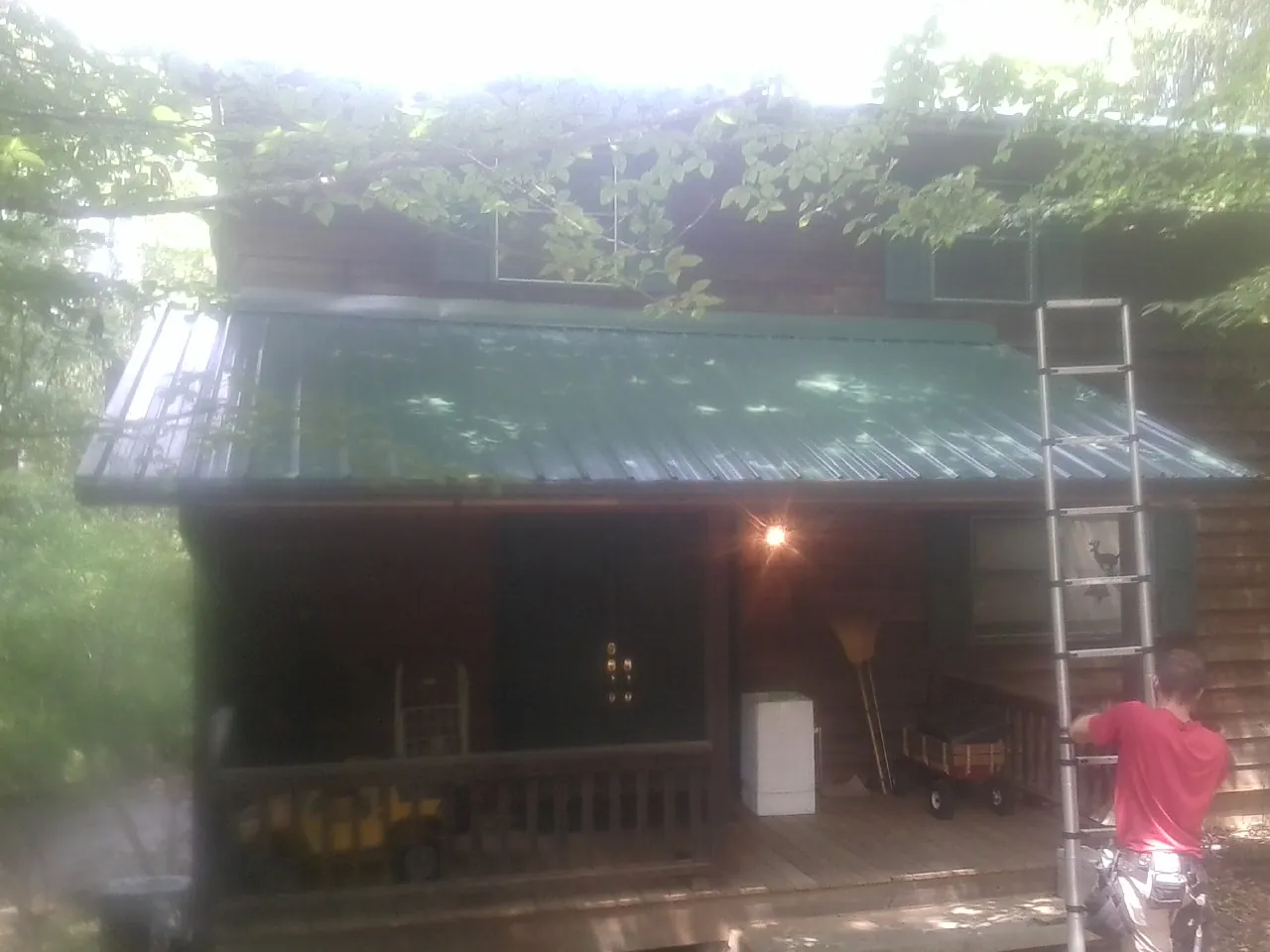 Worker on a ladder at the green porch roof of a wooded cabin in Prescott