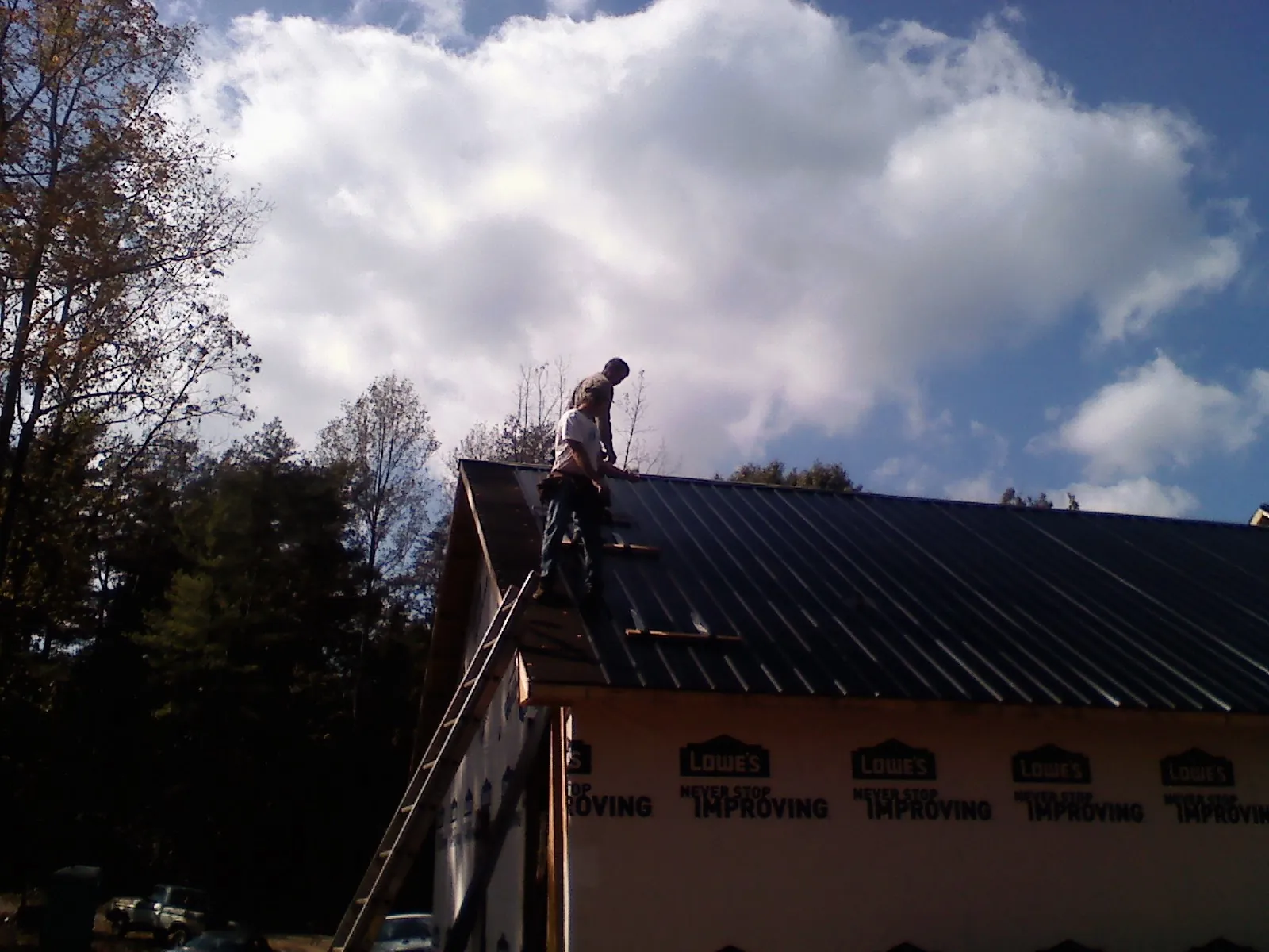 Roofer fastening dark metal panels high against a cloudy sky, from a Roof Inspection job in Prescott